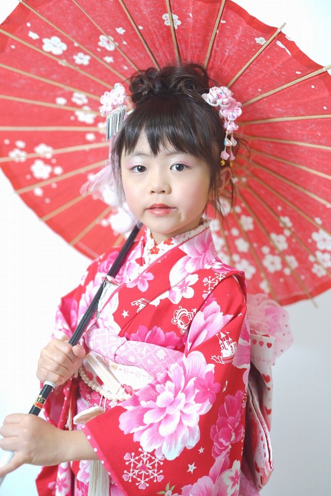 七五三の女の子が赤い和傘を持ってポーズを取っている写真