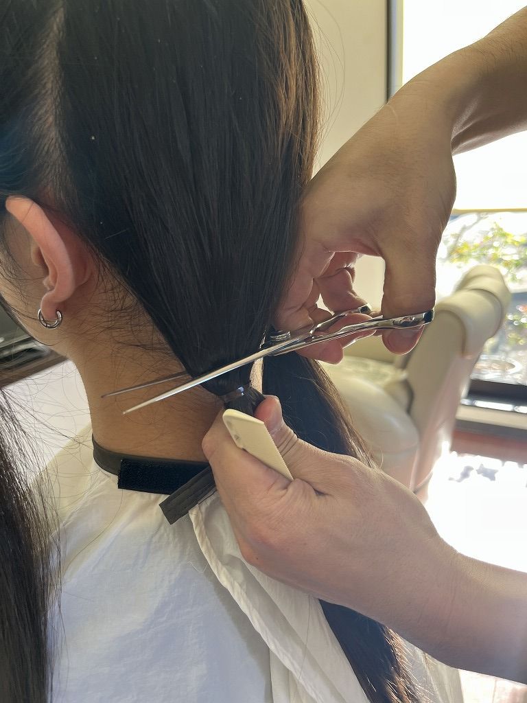 高校生男子のヘアドネーションで毛束をゴムで結びバッサリカットしている様子