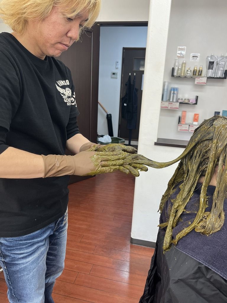 ハナヘナを塗布している施術中の写真。髪に丁寧にヘナをなじませている様子。