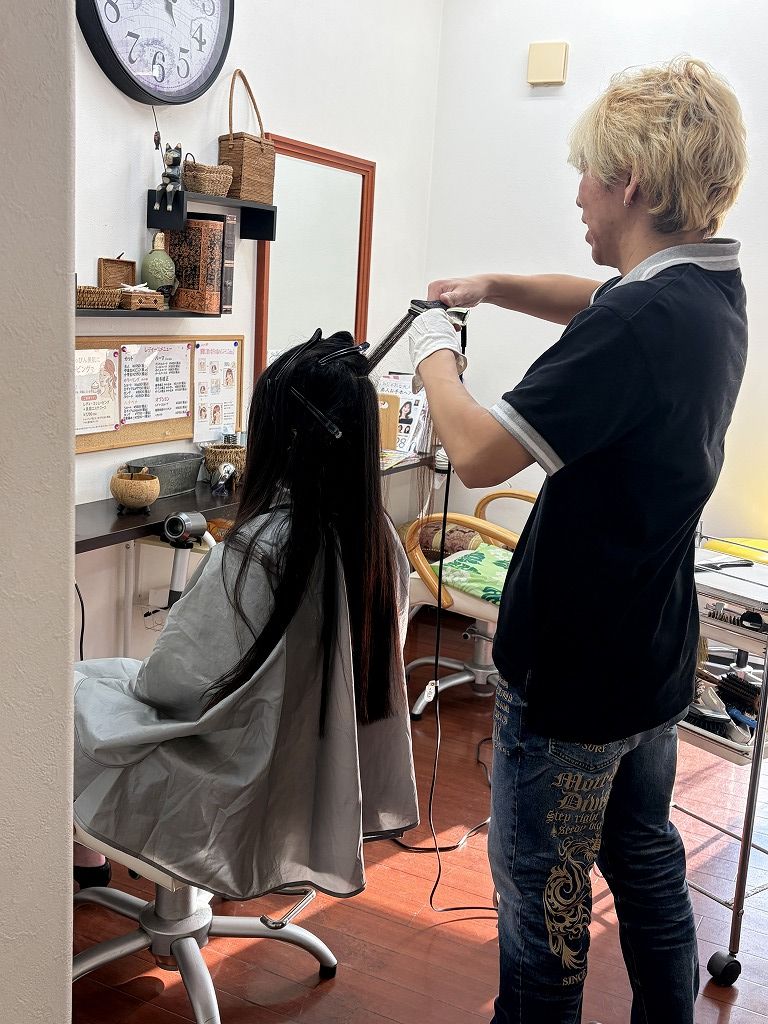 ロングヘアを細かく分けながら根元へアイロンを入れている縮毛矯正の工程